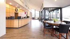 Un interior moderno con una recepción, un comedor con una mesa redonda y sillas, y ventanas amplias que ofrecen vistas al exterior.