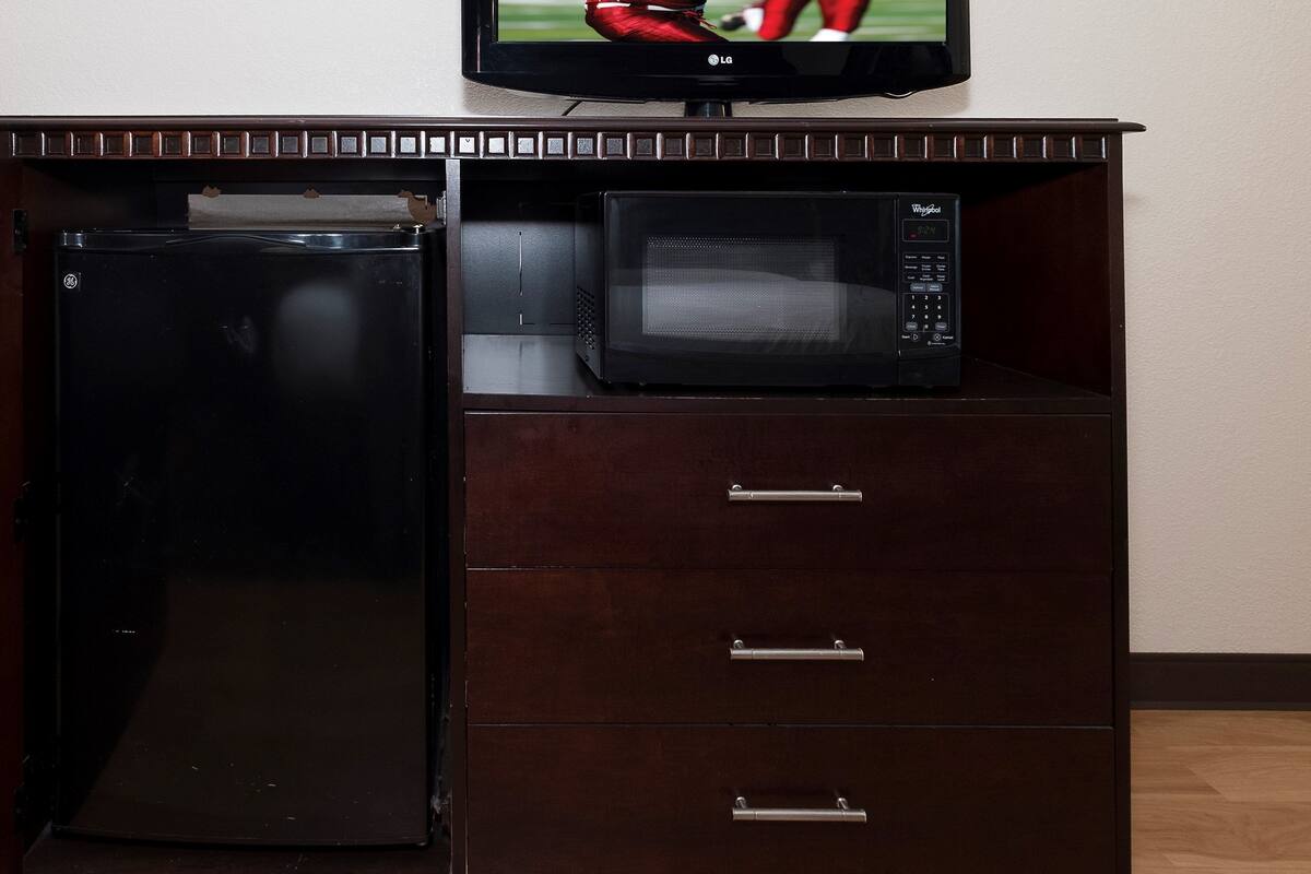 Una kitchenette con un refrigerador negro, un microondas y un televisor de pantalla plana encima.
