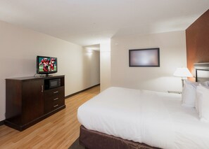 A hotel room with a bed, a television on a wooden cabinet, a wall-mounted picture, and a bedside lamp.