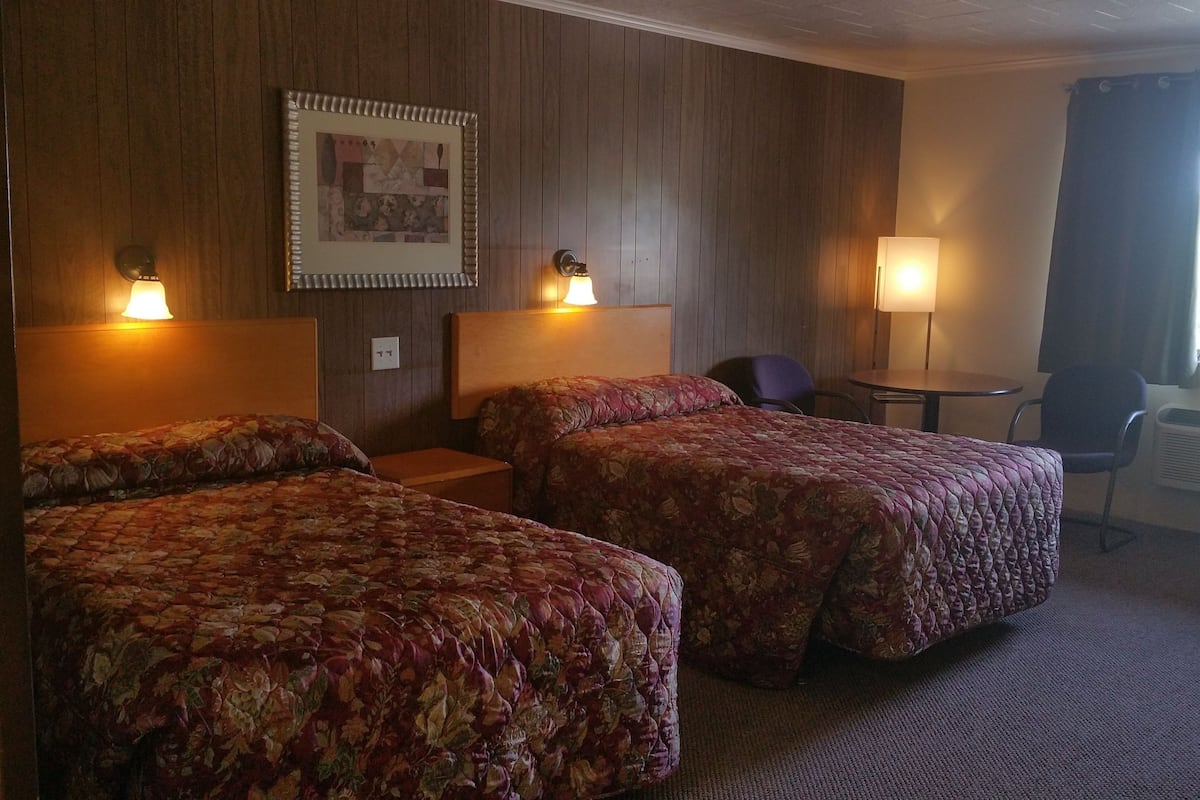 Habitación de hotel con dos camas, una mesita y una silla.
