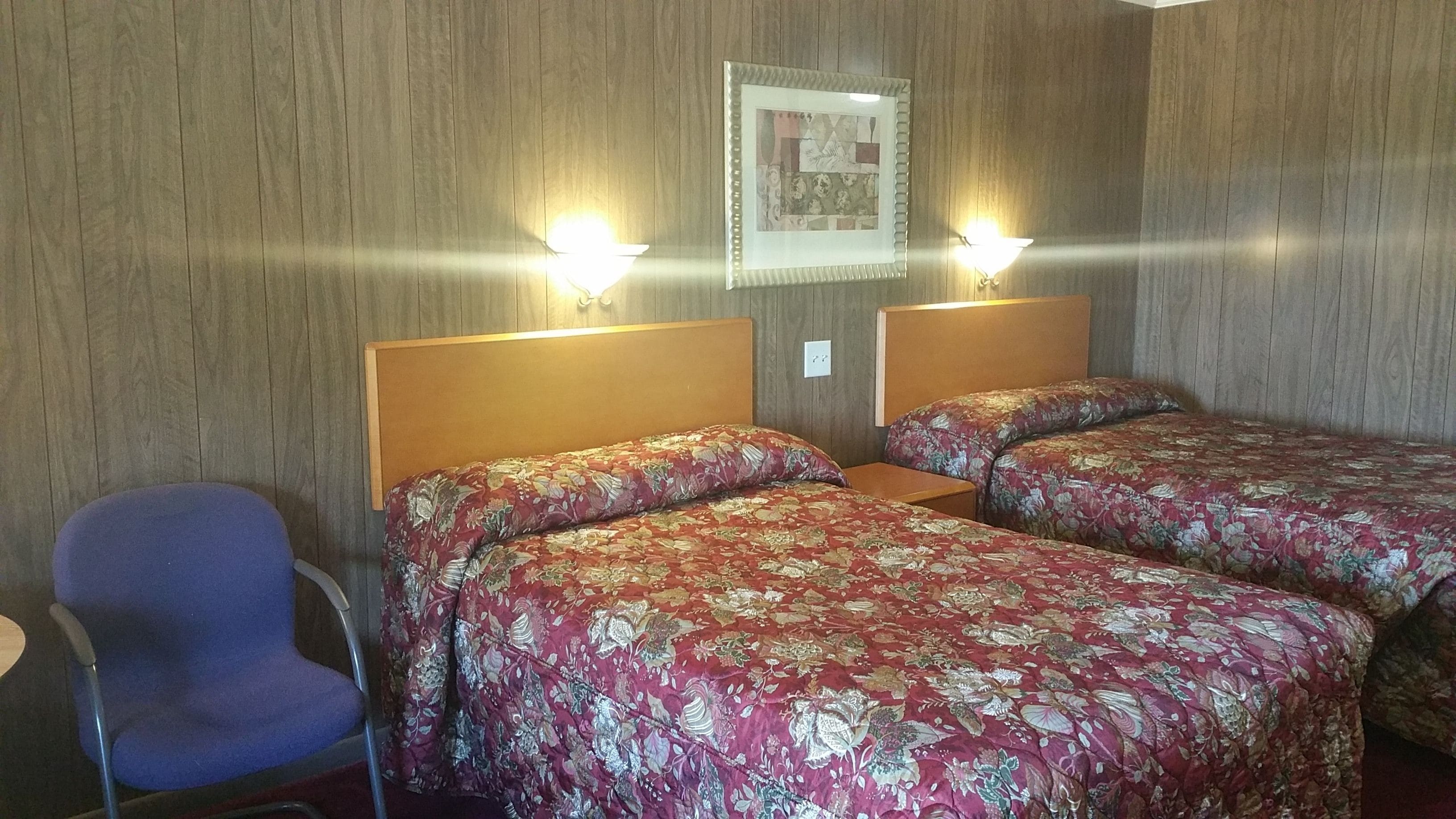 A hotel room with two beds, a chair, and two wall-mounted lamps.