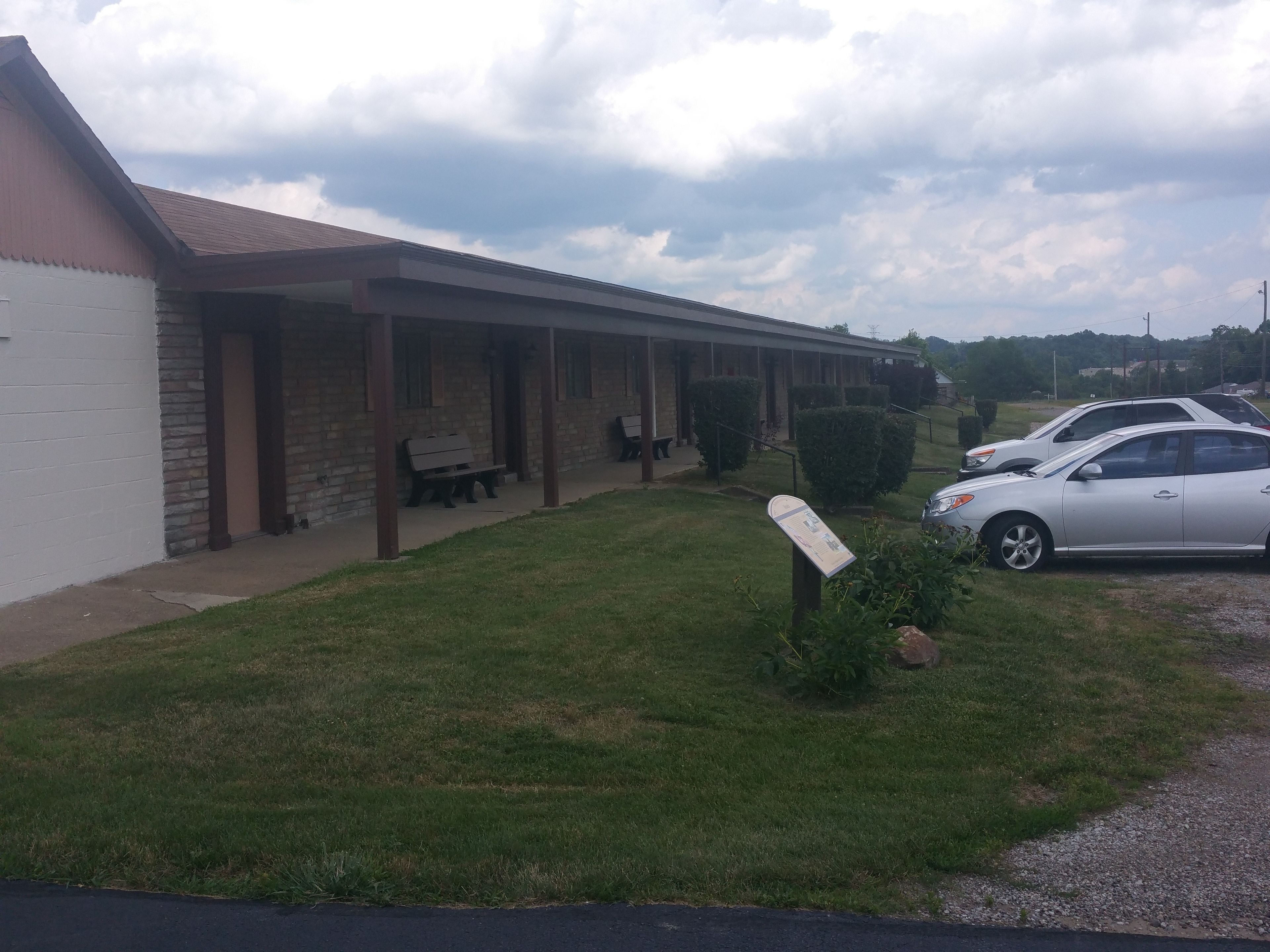 A motel with a covered parking area, a grassy lawn, and a signboard.