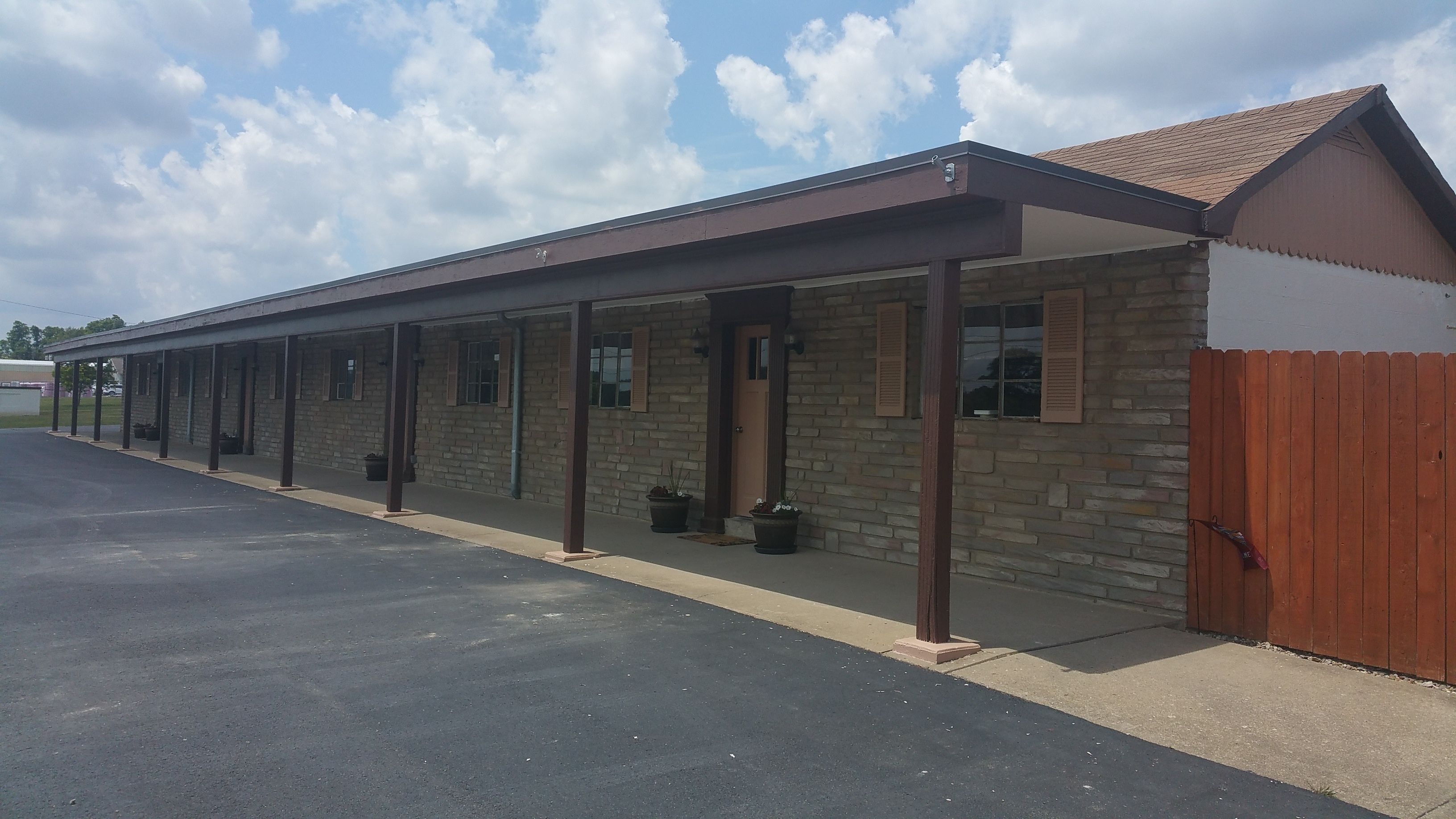 A row of single-story motel rooms with individual entrances, a covered parking area, and a wooden fence.