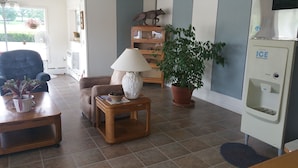 Un salon comprenant un canapé, une table basse avec une lampe, une plante en pot et un distributeur de glaçons fixé au mur.