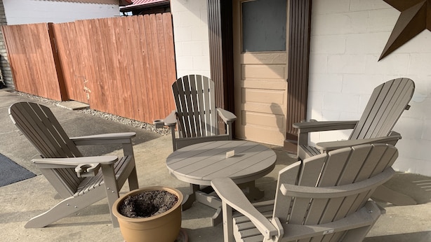Un espace patio avec des fauteuils Adirondack et une table ronde, un pot de fleurs et une clôture en bois en arrière-plan.
