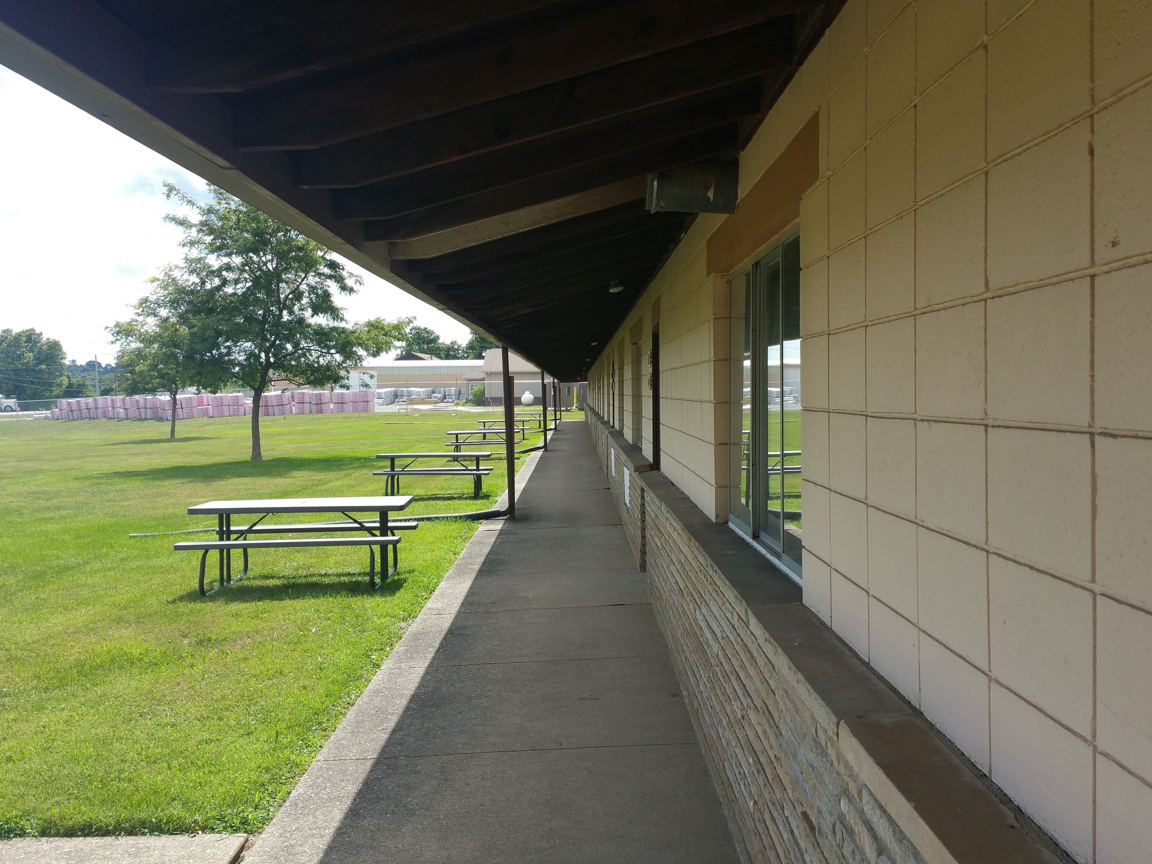 A covered outdoor area with picnic tables and a grassy field.