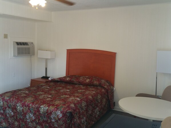 Een hotelkamer met een éénpersoonsbed, een nachtkastje met een lamp, een ronde tafel en een airconditioning aan de muur.