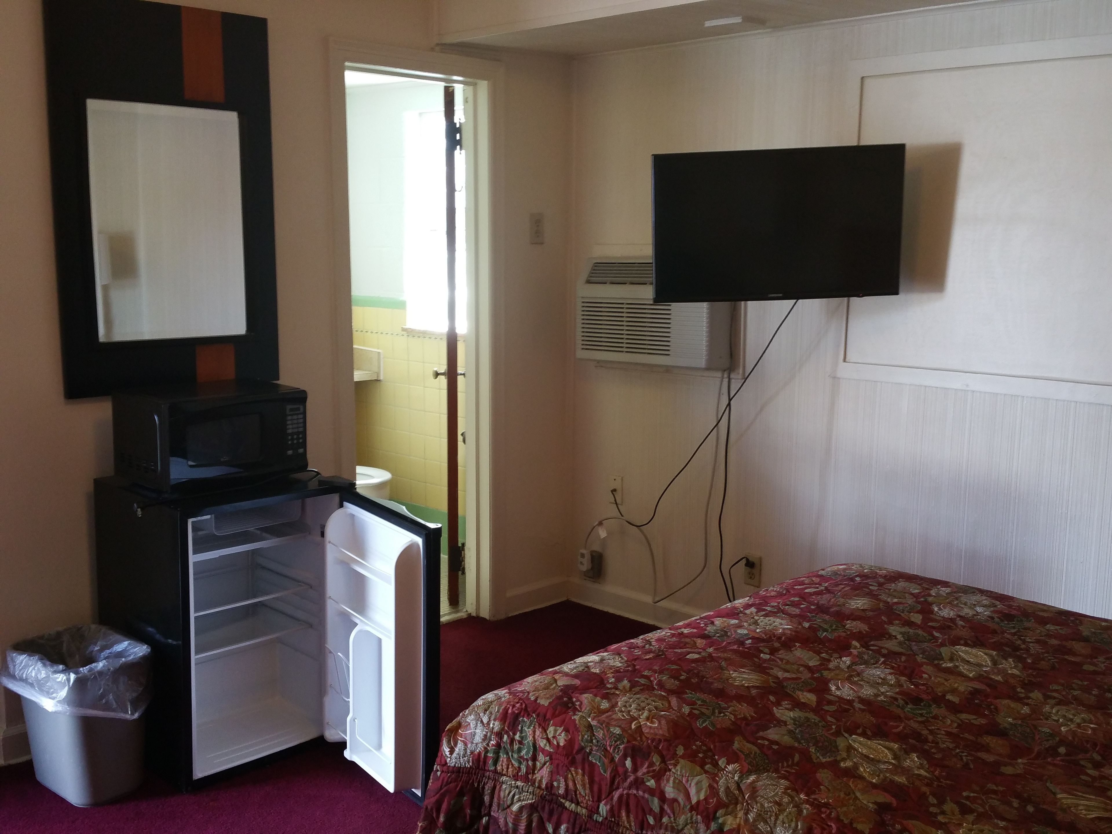 Ein Hotelzimmer mit einem Bett, einem an der Wand befestigten Fernseher, einer Minikühlschrank, einer Mikrowelle und einem Mülleimer.