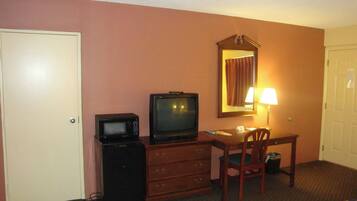 A hotel room with a television, a small desk, a chair, a dresser, and a mirror.