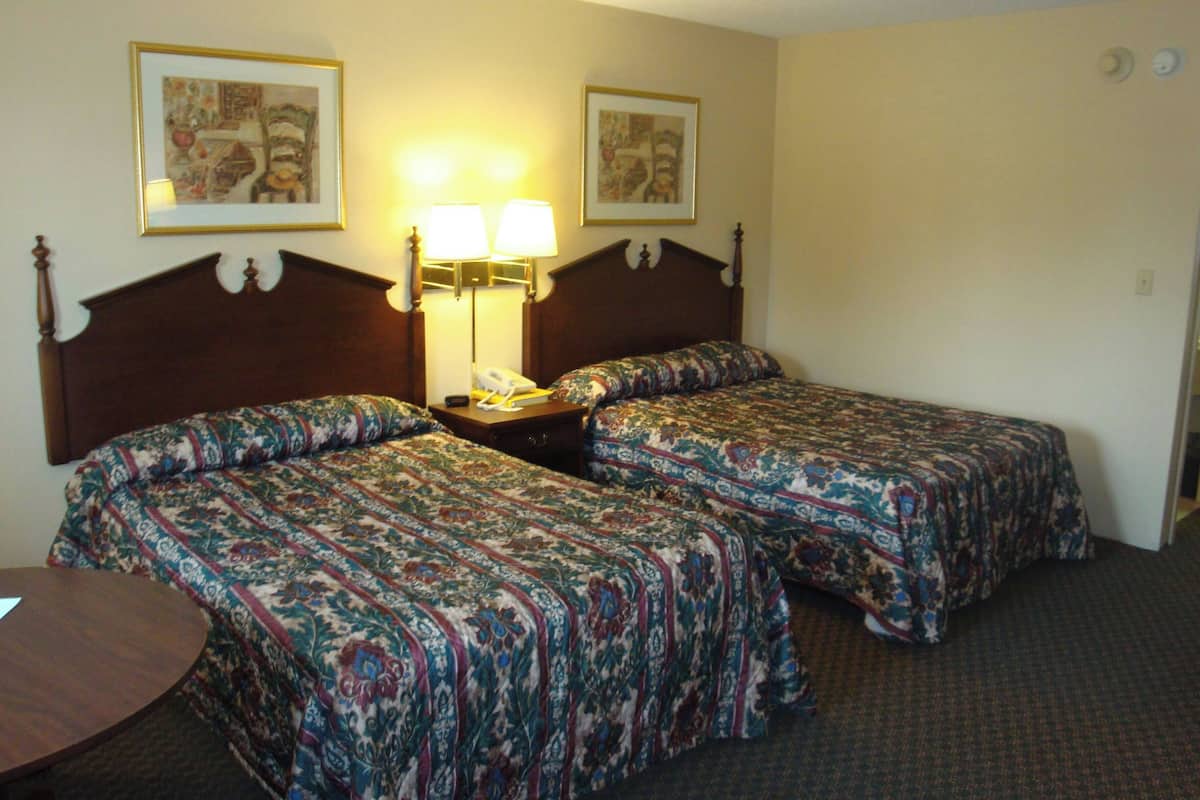 A hotel room with two beds, a bedside table with a lamp, a phone, and two framed pictures on the wall.