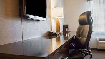 Une chambre d’hôtel équipée d’un téléviseur à écran plat fixé au mur, d’un bureau avec une lampe, d’une machine à café et d’un fauteuil en cuir.
