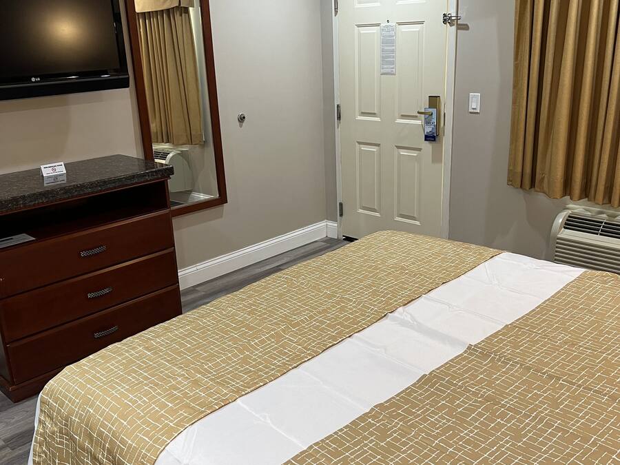 A hotel room with a bed, a dresser, a television, a door, and an air conditioning unit.