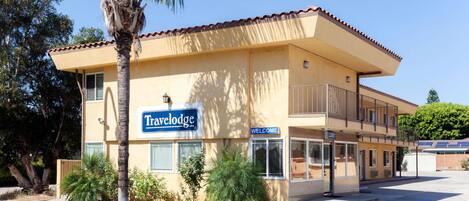 A Travelodge hotel with a beige facade, a balcony on the second floor, and a palm tree in the foreground.