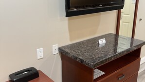 A room with a flat-screen TV mounted on the wall, a wooden desk with a tissue box, and a wooden cabinet with drawers. - Travelodge by Wyndham Brea (Brea)