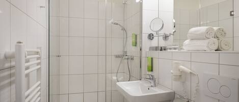 Un baño moderno con cabina de ducha de vidrio, lavamanos blanco y un perchero para toallas.
