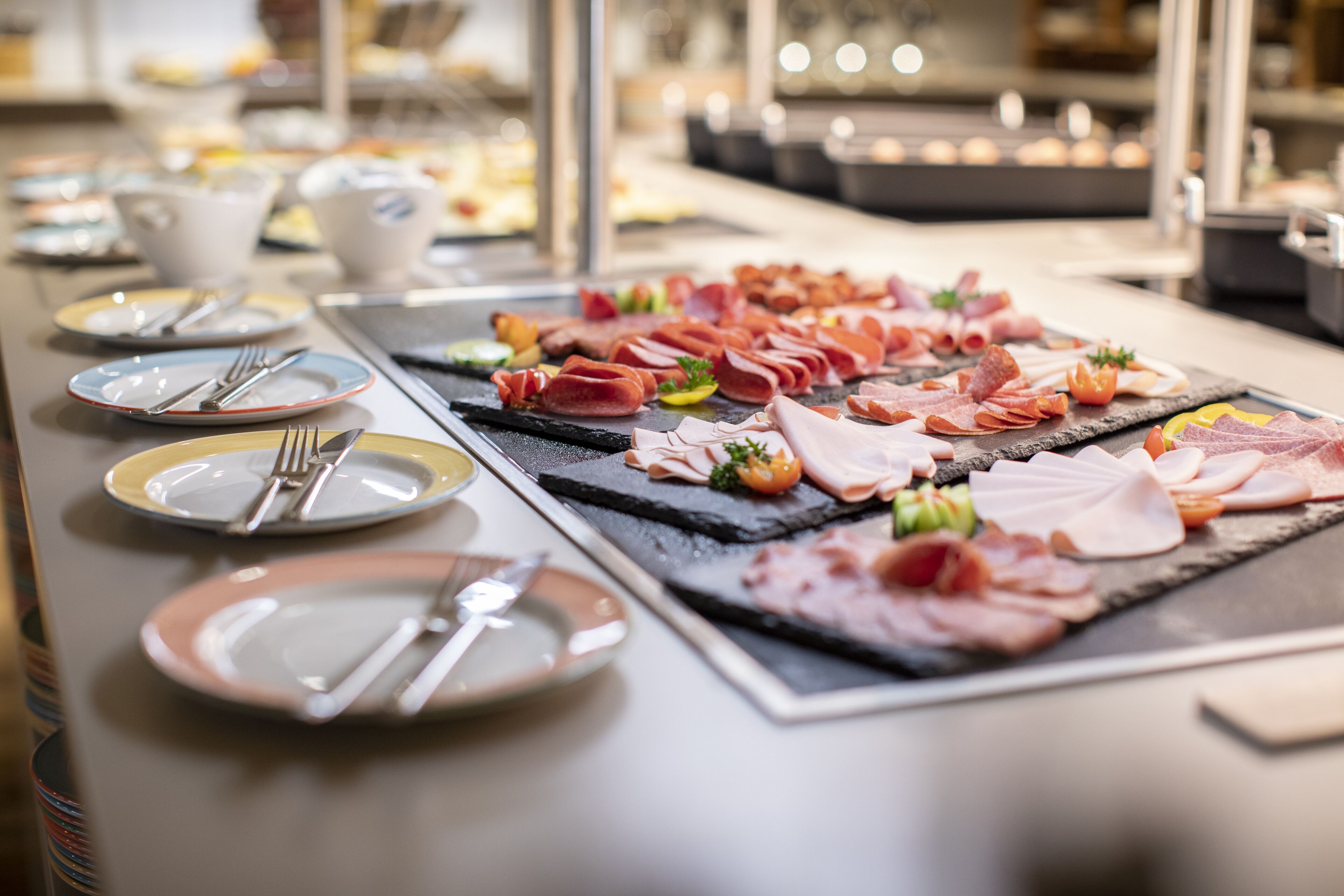 A buffet with various meats and garnishes on black slate boards.