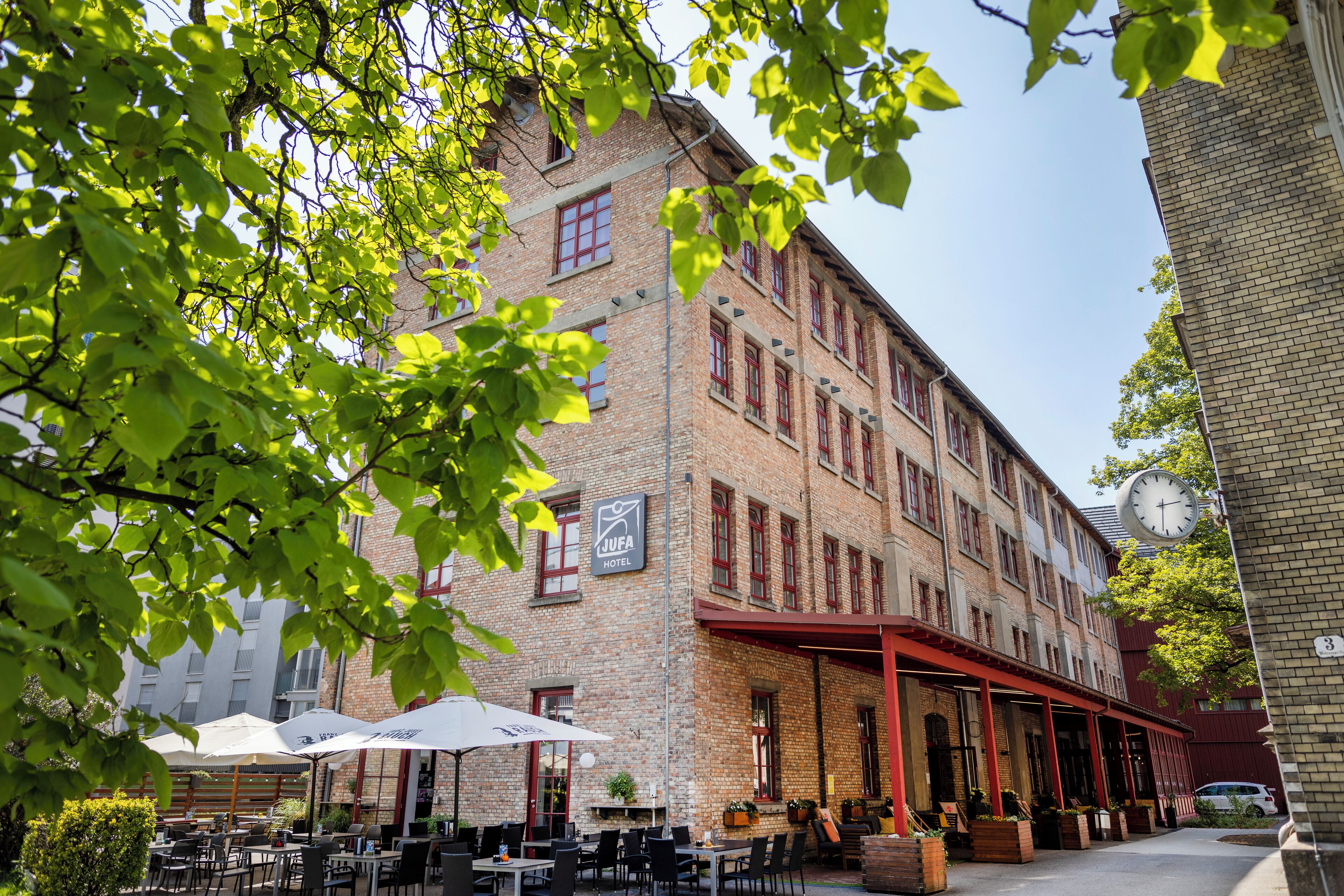 Un hôtel doté d’une terrasse, d’une façade en briques et d’une horloge.