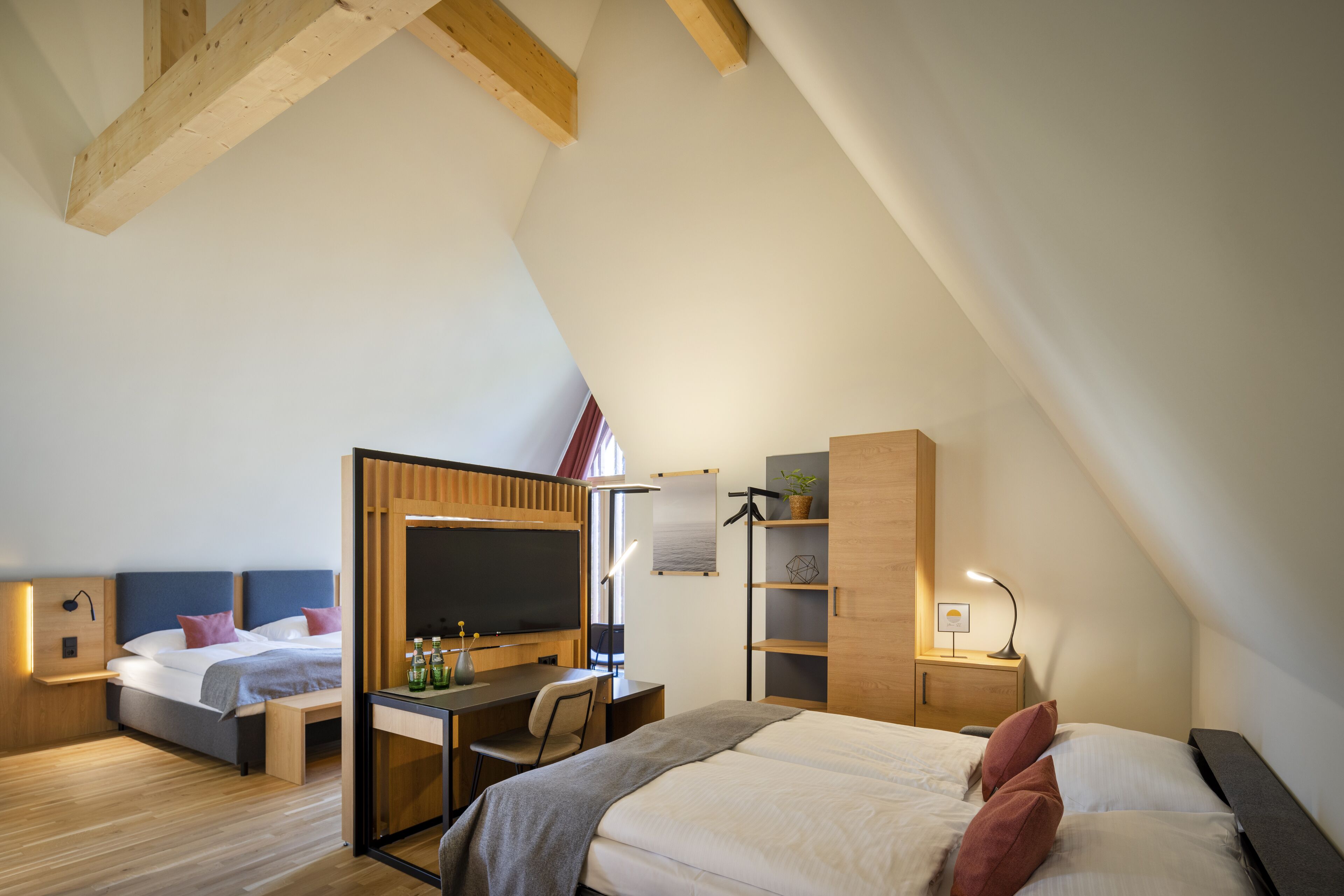 Ein modernes Hotelzimmer mit Schlafgalerie, Schreibtisch, Stuhl, Fernseher und Bücherregal.