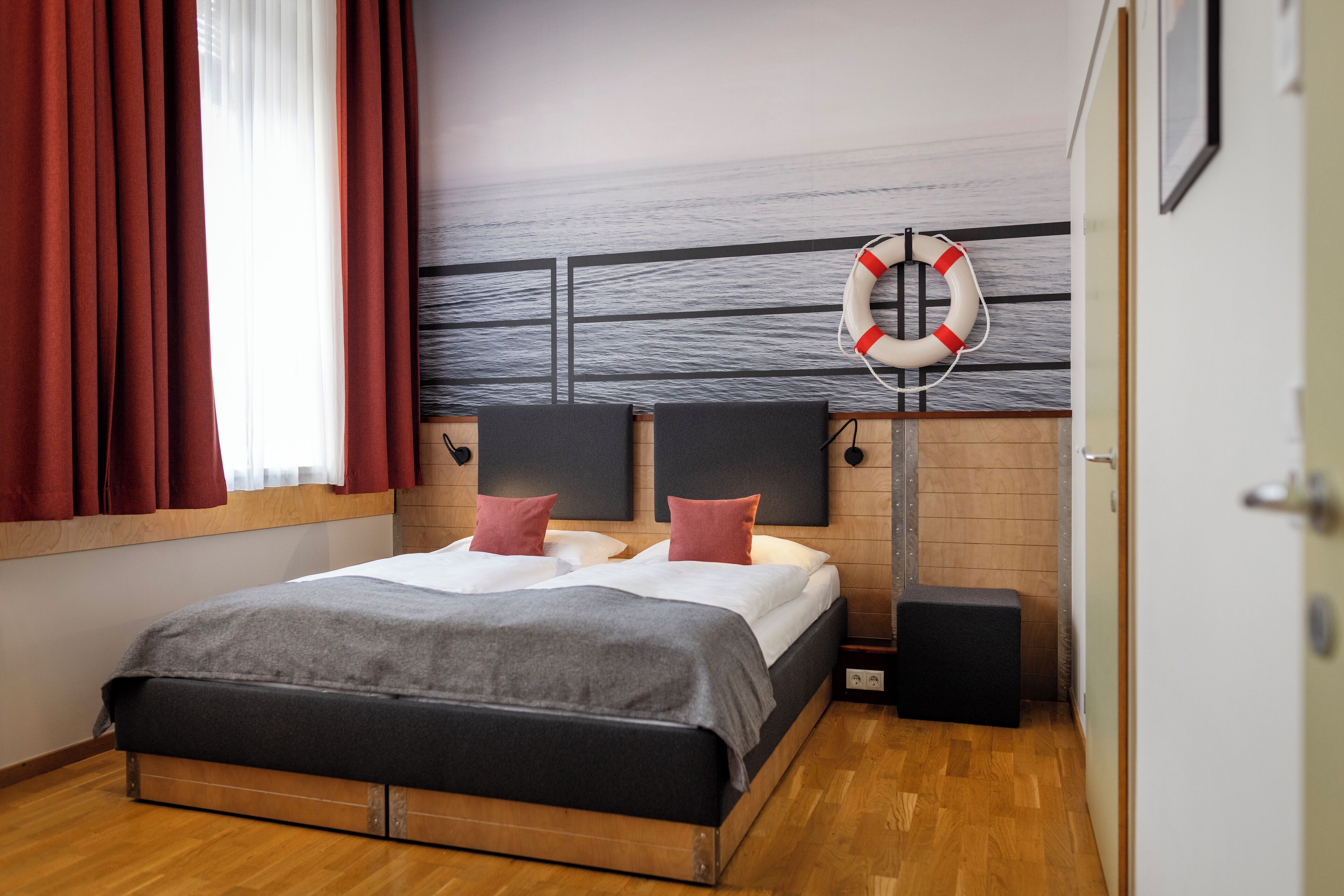 Un dormitorio con una cama, dos almohadas, un salvavidas, un altavoz y una ventana con cortinas.