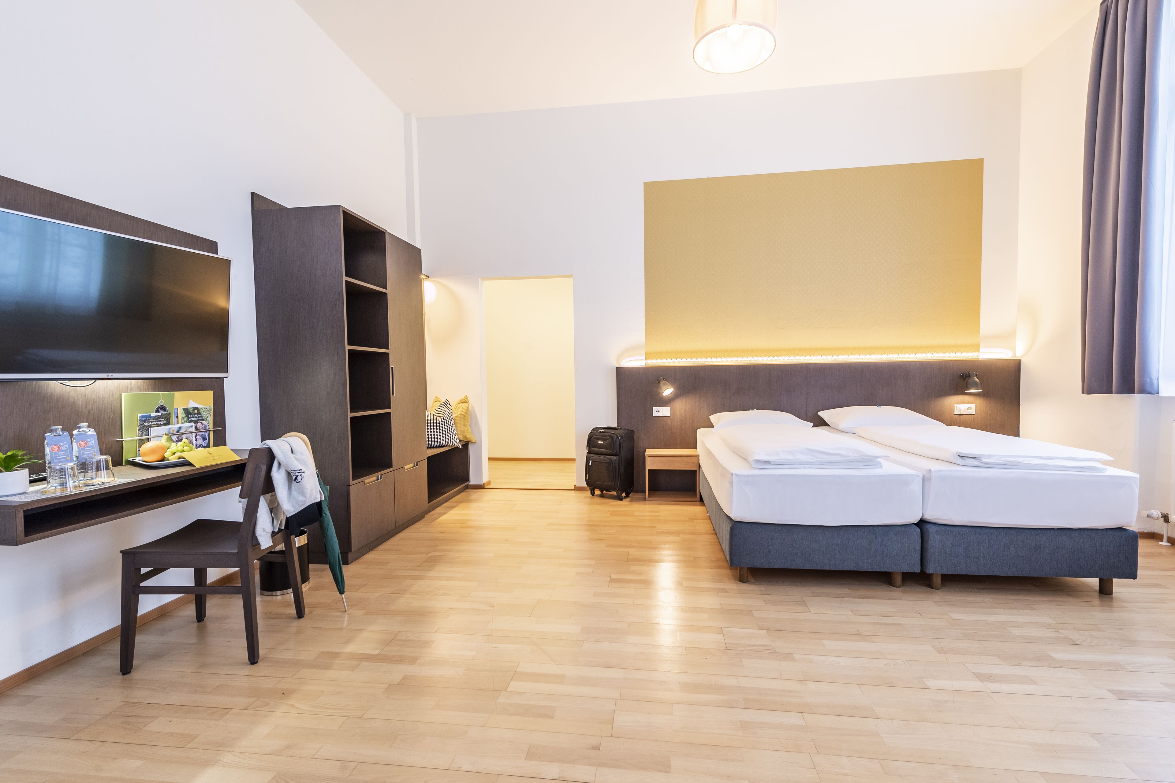 A hotel room with a bed, a desk, a TV, and a wardrobe.