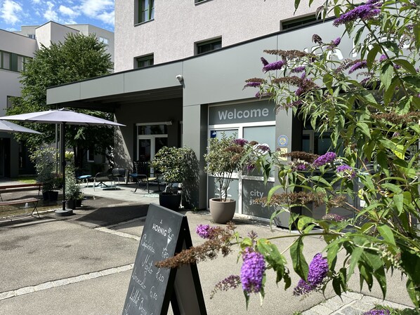 An outdoor seating area with a chalkboard menu, potted plants, and a 'Welcome' sign.