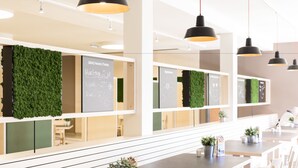 A modern restaurant with green wall decorations, black pendant lights, and neatly arranged tables and chairs.