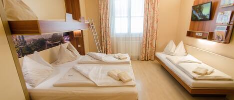 Habitación de hotel con dos camas individuales, una litera de madera, un televisor montado en la pared y una ventana con cortinas.