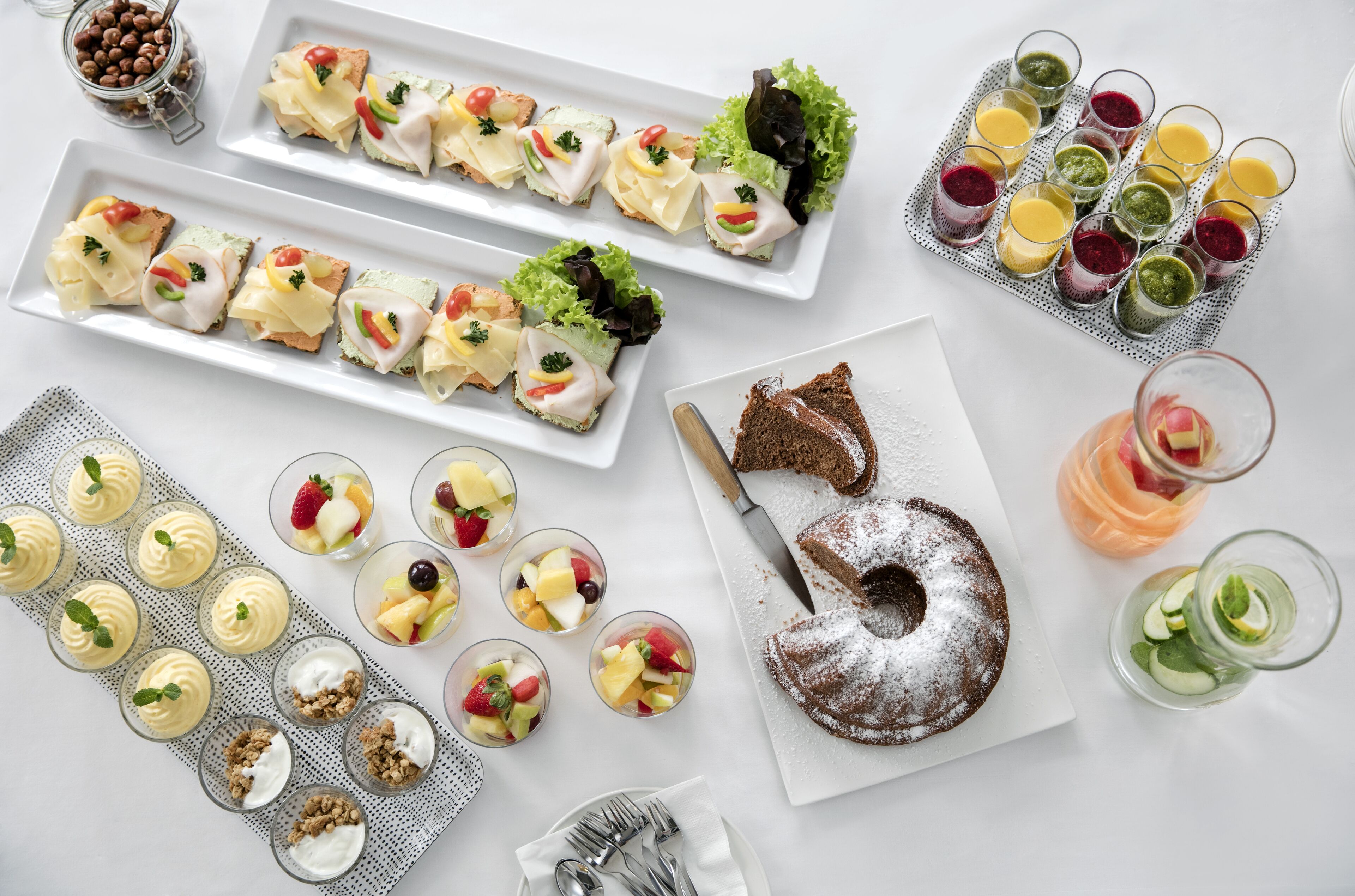 A variety of food items including sandwiches, fruit cups, and a cake on a white table.