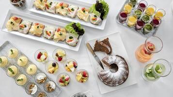 A variety of food items including sandwiches, fruit cups, and a cake on a white table.