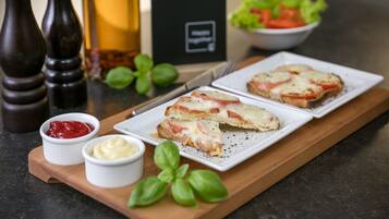 A wooden serving board with two slices of pizza, a small bowl of ketchup, a small bowl of butter, and a basil leaf.