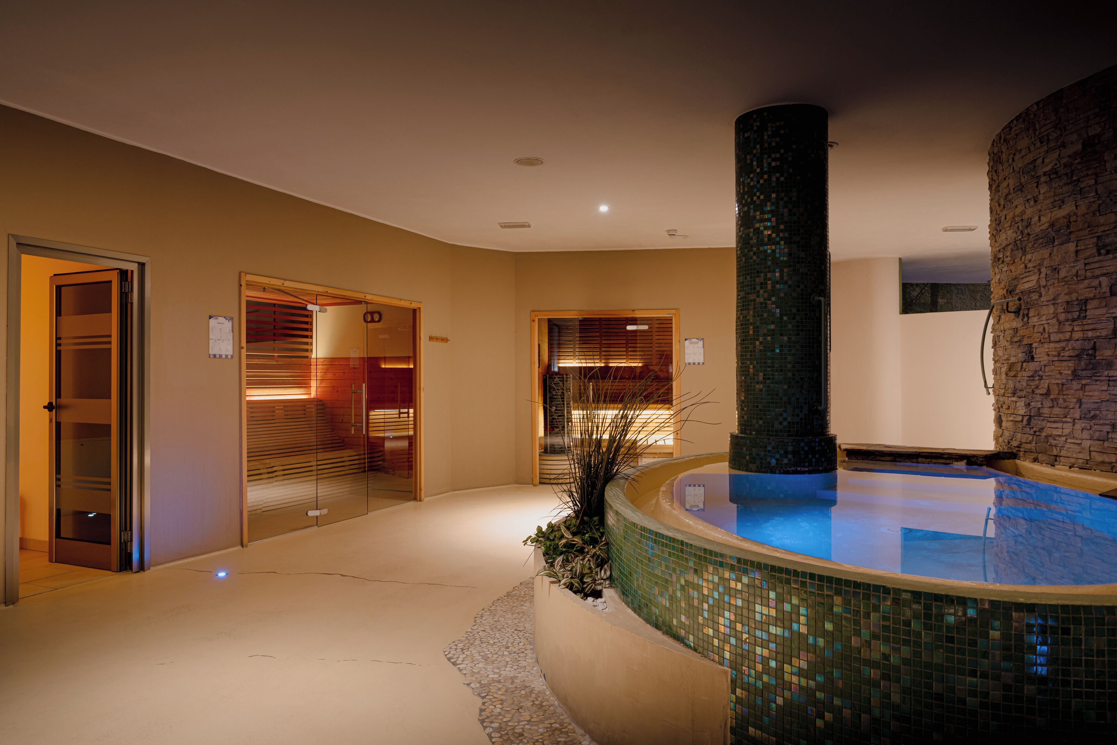 Un hall d’hôtel moderne avec une piscine centrale, des portes en verre et un mur en pierre.