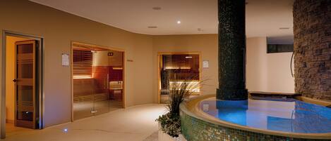 A modern hotel lobby with a central pool, glass doors, and a stone wall.
