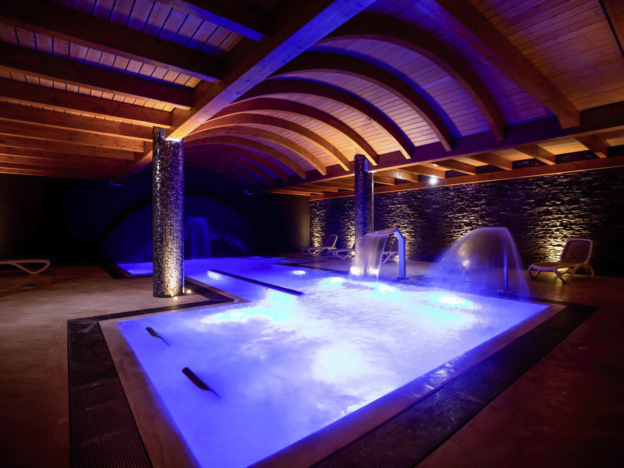 Ein Wellnessbereich mit Whirlpool, zwei Wasserfällen und Liegestühlen.