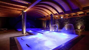 Ein Wellnessbereich mit Whirlpool, zwei Wasserfällen und Liegestühlen.