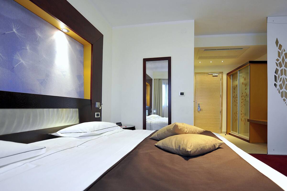 Une chambre d’hôtel comprenant un lit, un miroir, une armoire et une porte donnant sur une autre pièce.