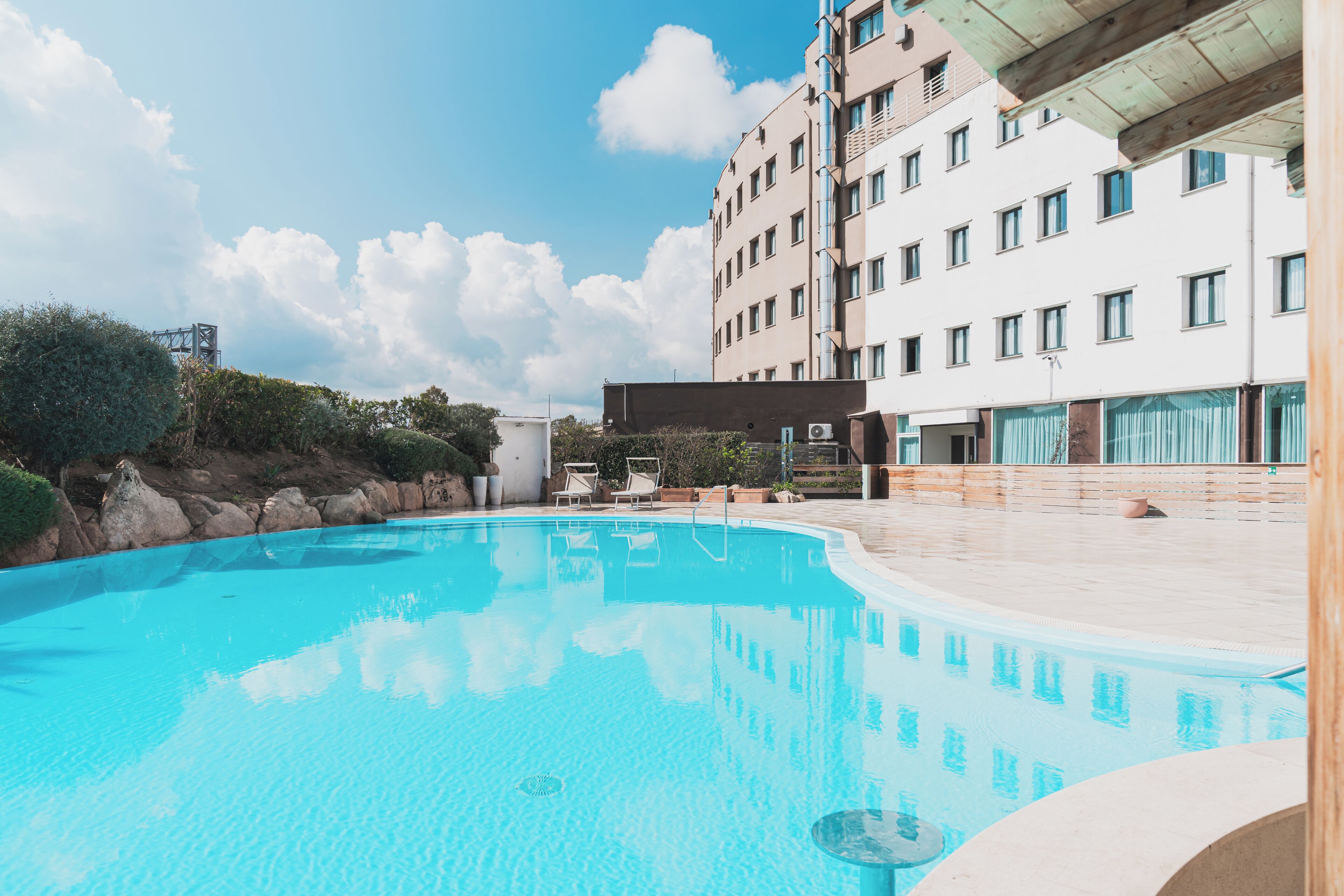 Una piscina con lettini e sdraio, con un edificio con diverse finestre sullo sfondo.