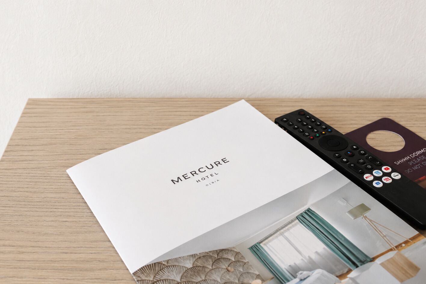 Une brochure d’hôtel Mercure, une télécommande et une pancarte en bois indiquant : « SILENCE ! LAISSEZ-NOUS DORMIR ».