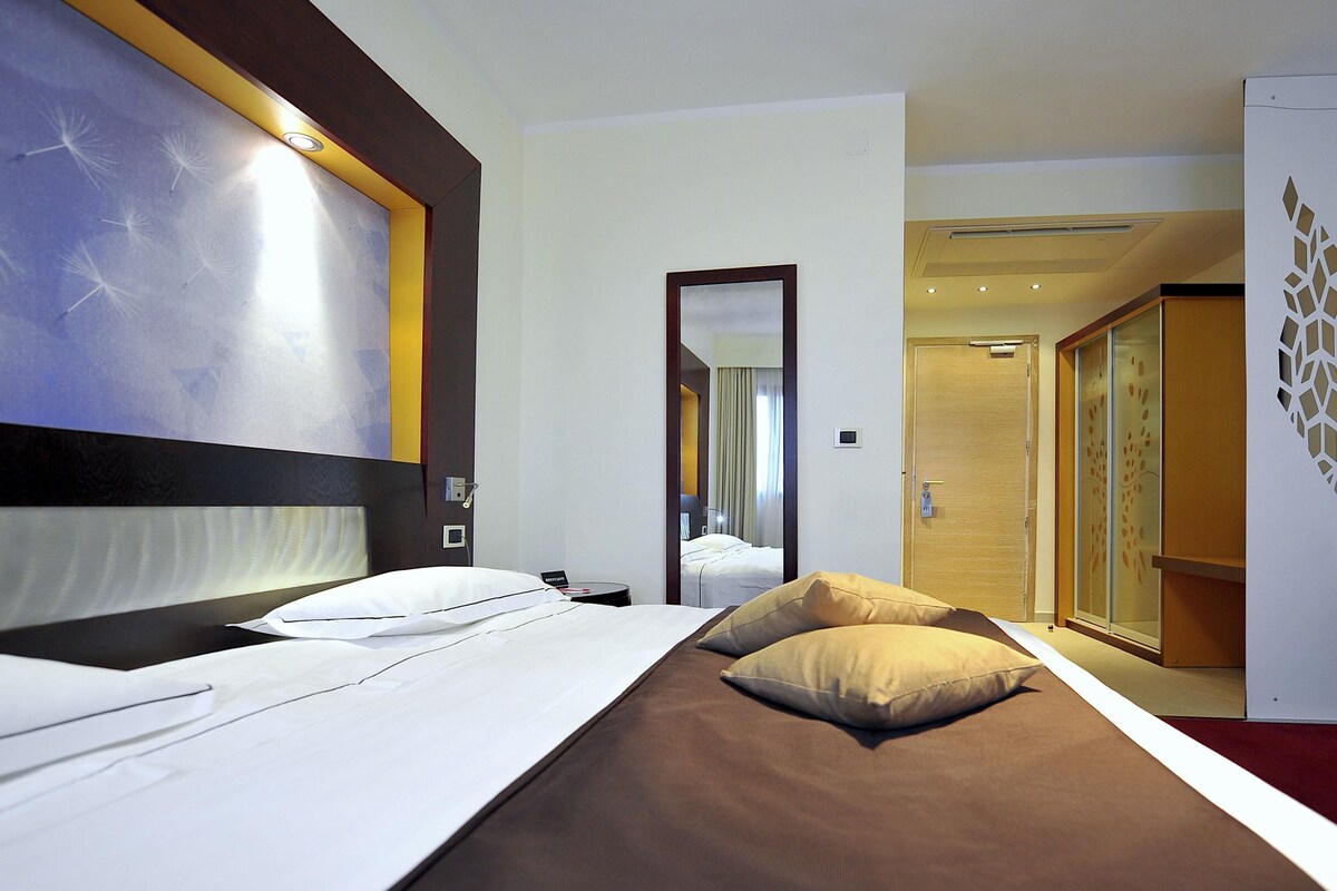 Une chambre d’hôtel comprenant un lit, un miroir, une armoire et une porte donnant sur une autre pièce.