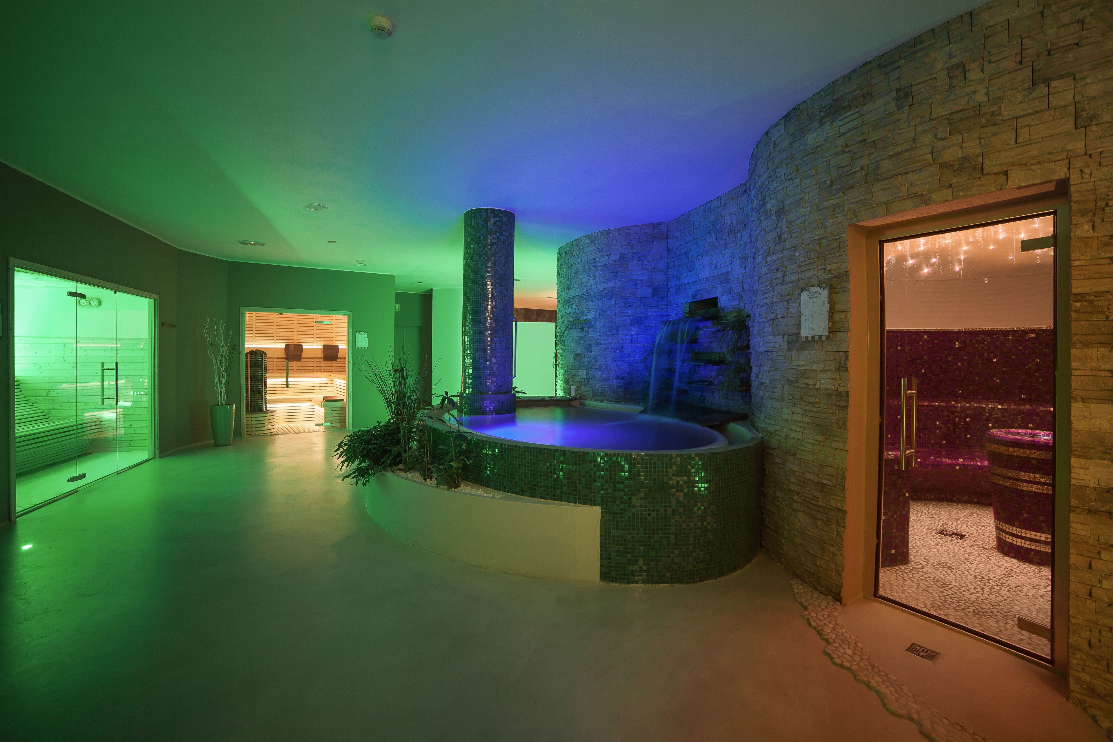 A modern interior with a circular water feature, a stone wall, and a glass door leading to a room with a patterned floor.