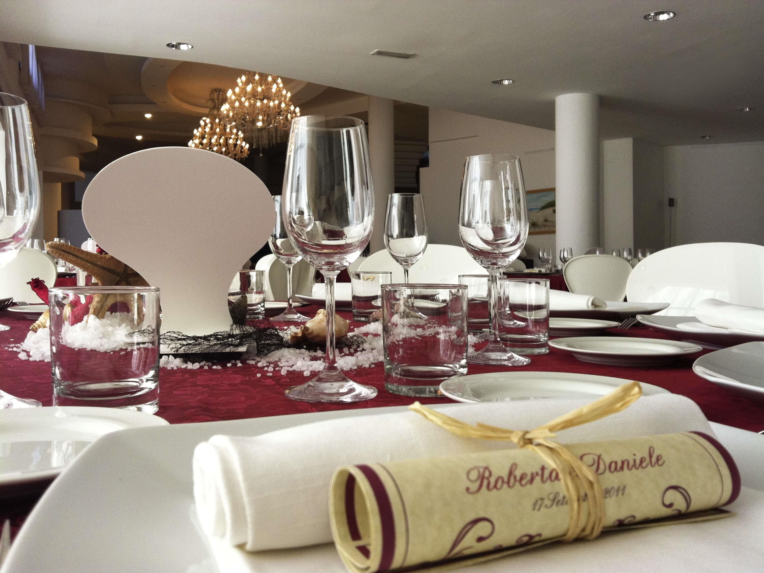 A dining table set with wine glasses, plates, and a rolled napkin tied with a ribbon.