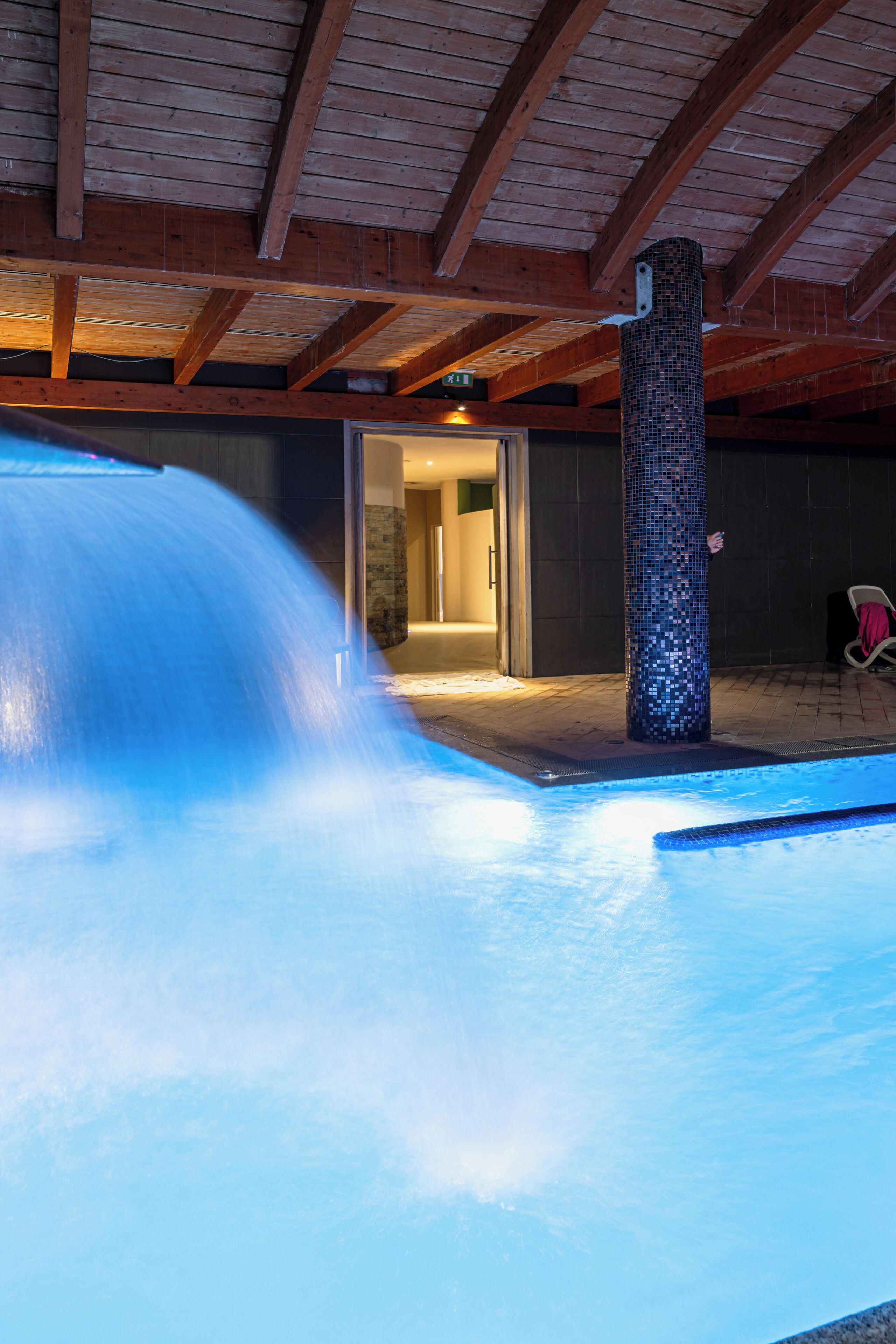 A pool with a water feature, a tiled pillar, and a doorway leading to an interior space.