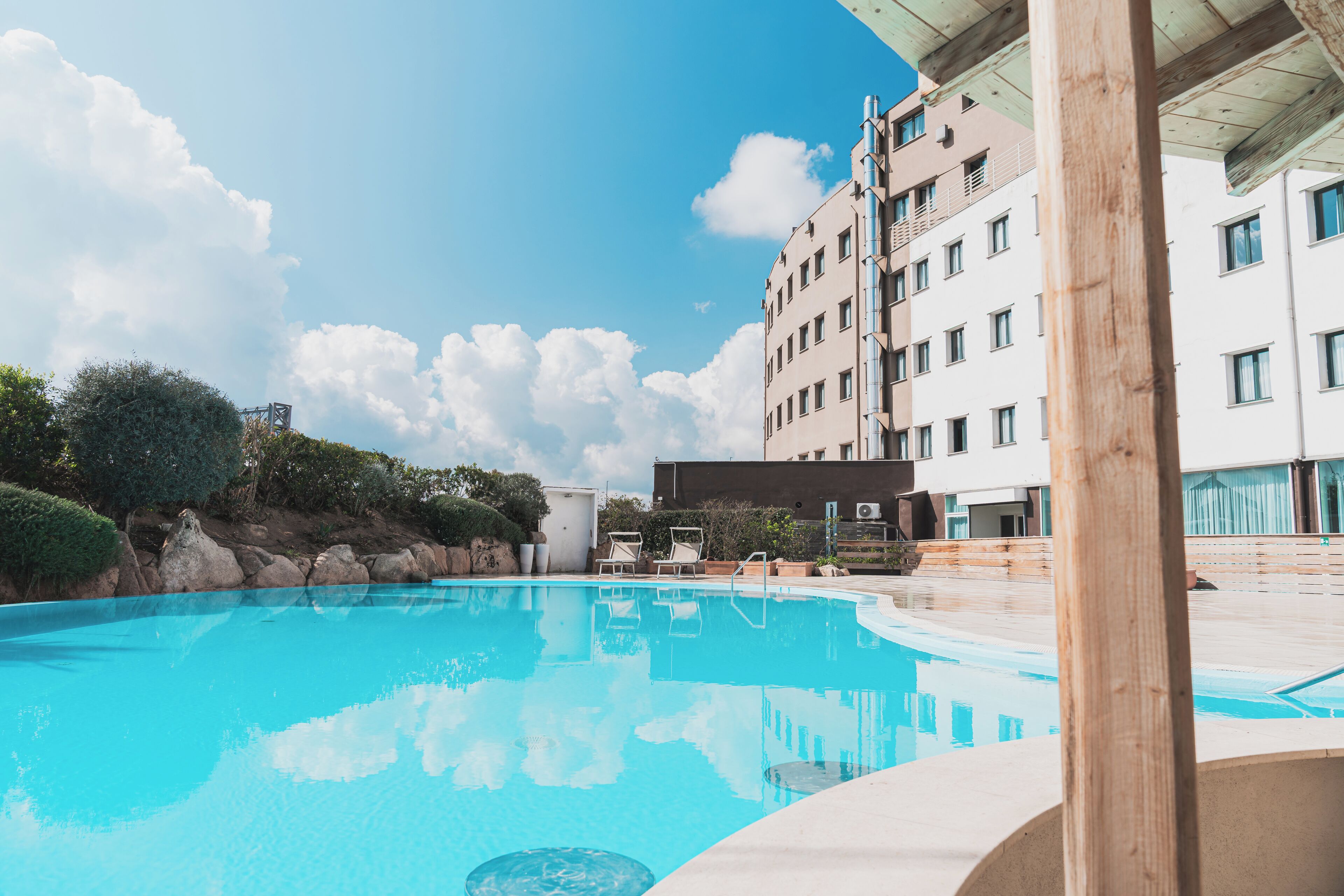 Una piscina con agua azul cristalina, rodeada por una terraza de madera y un edificio con varias ventanas y balcones.