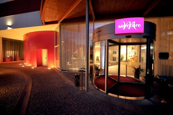Ein moderner Hotel Eingang mit Glastür, roter Außenbeleuchtung und einem sichtbaren Empfangsbereich im Inneren.
