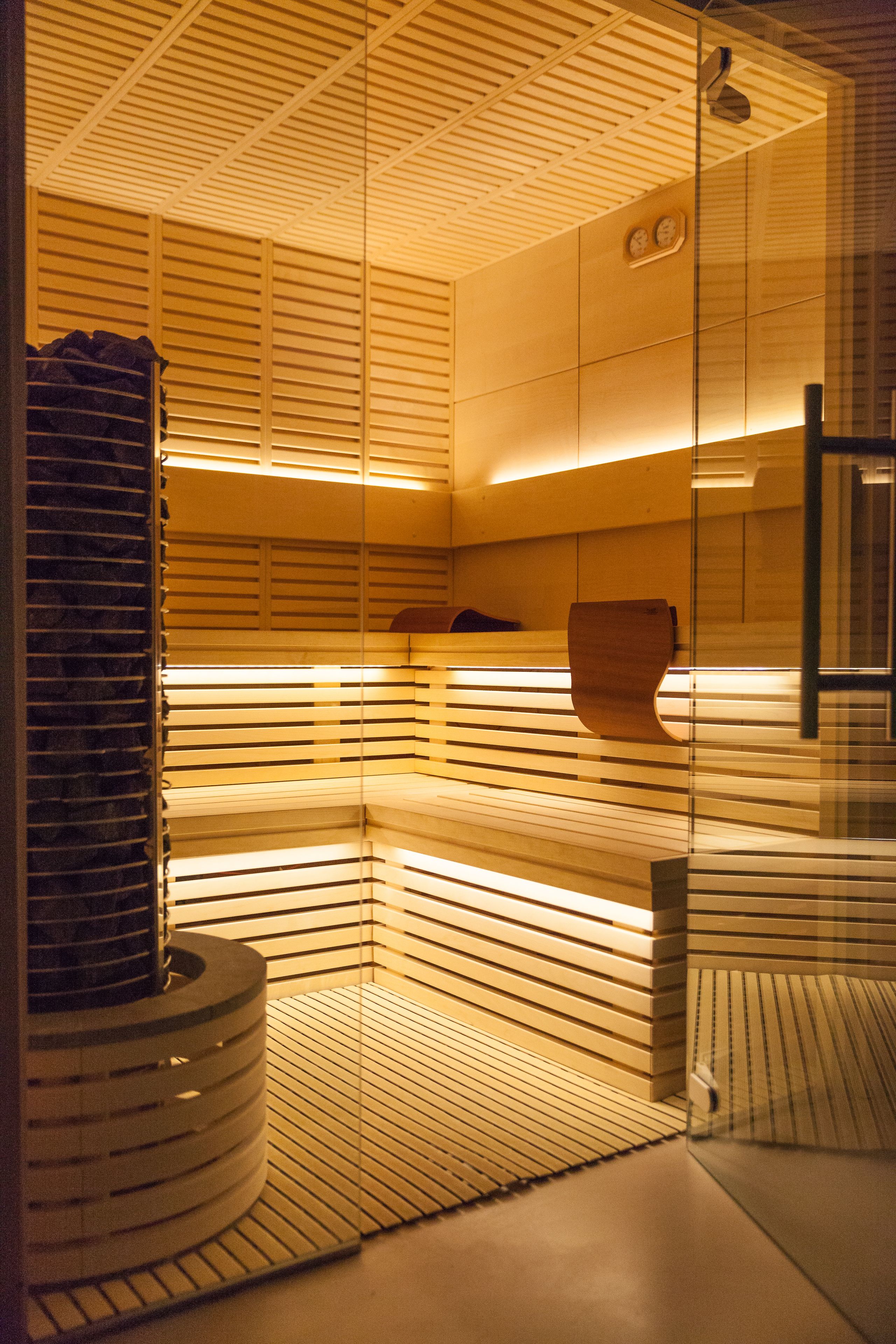 Un sauna moderne et bien éclairé, doté d’un plafond et de murs en bois à lattes, d’un banc en bois et d’une porte en verre.