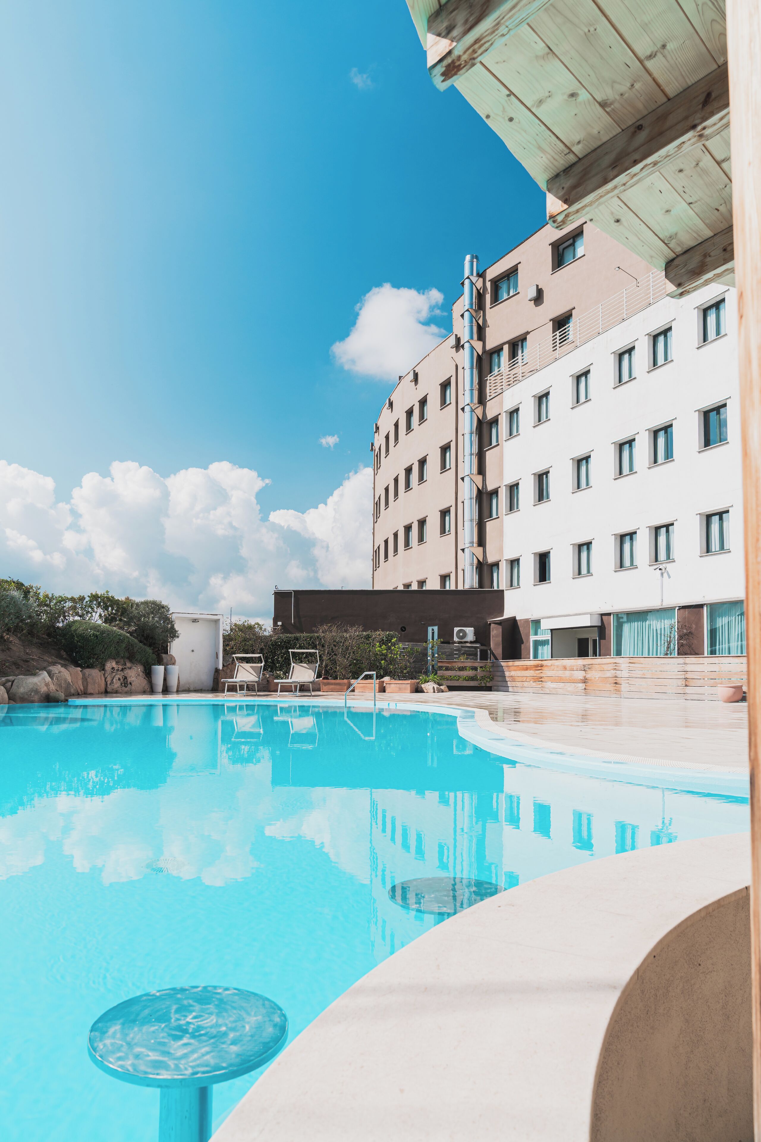 Una piscina con sillas de descanso y un edificio con varias ventanas al fondo.