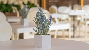 Un restaurant avec des tables et des chaises blanches, un toit de chaume et un pot de lavande posé sur la table.