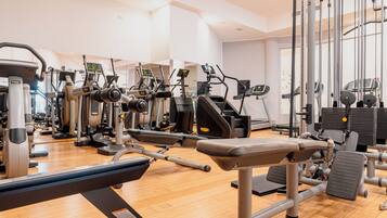 A gym with various exercise machines, a wooden floor, and a large window.