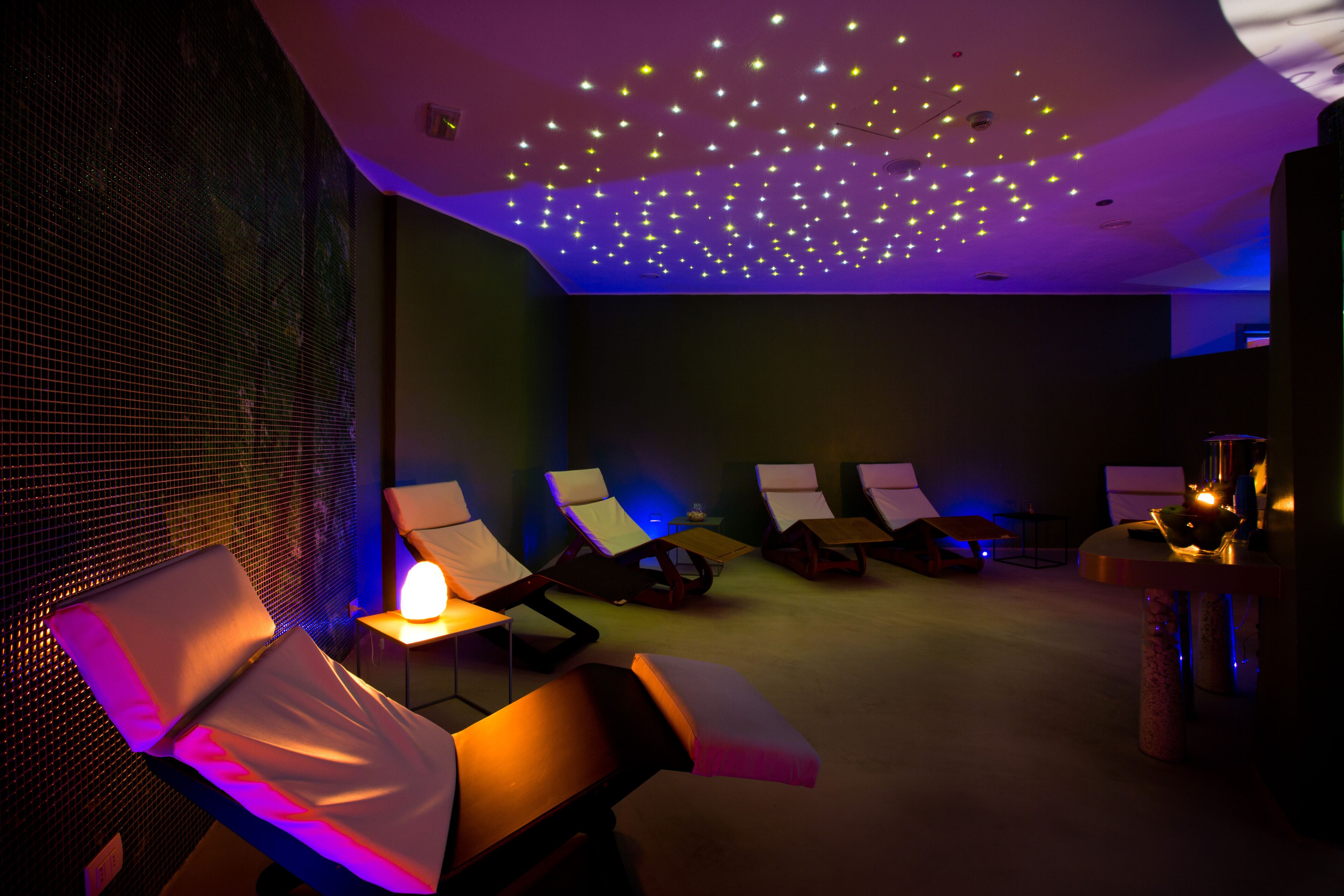 A spa room with reclining chairs, a massage table, and a ceiling with a star-like light pattern.