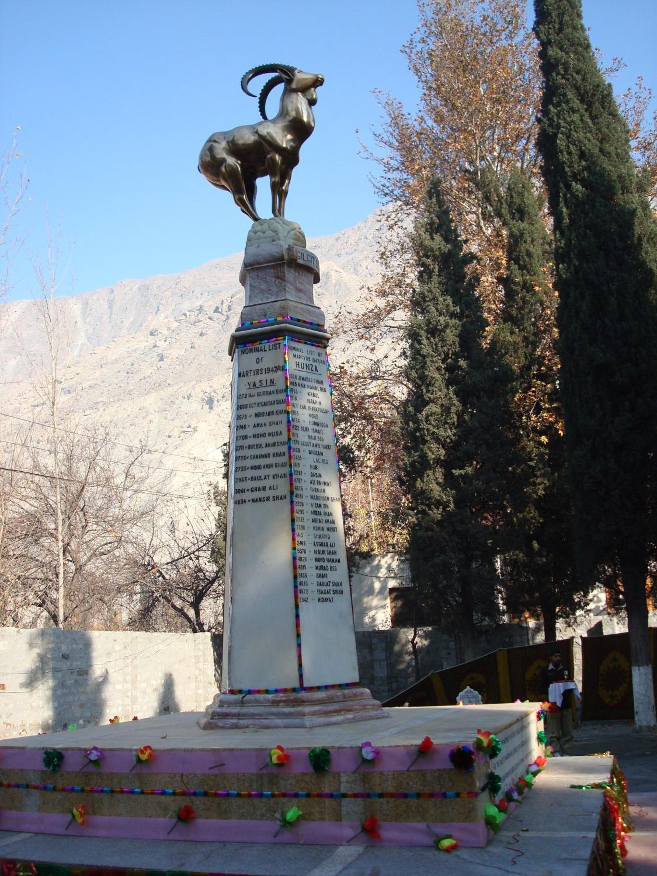 Un monumento con una estatua de cabra, una lista de nombres y una escalera con decoraciones coloridas.