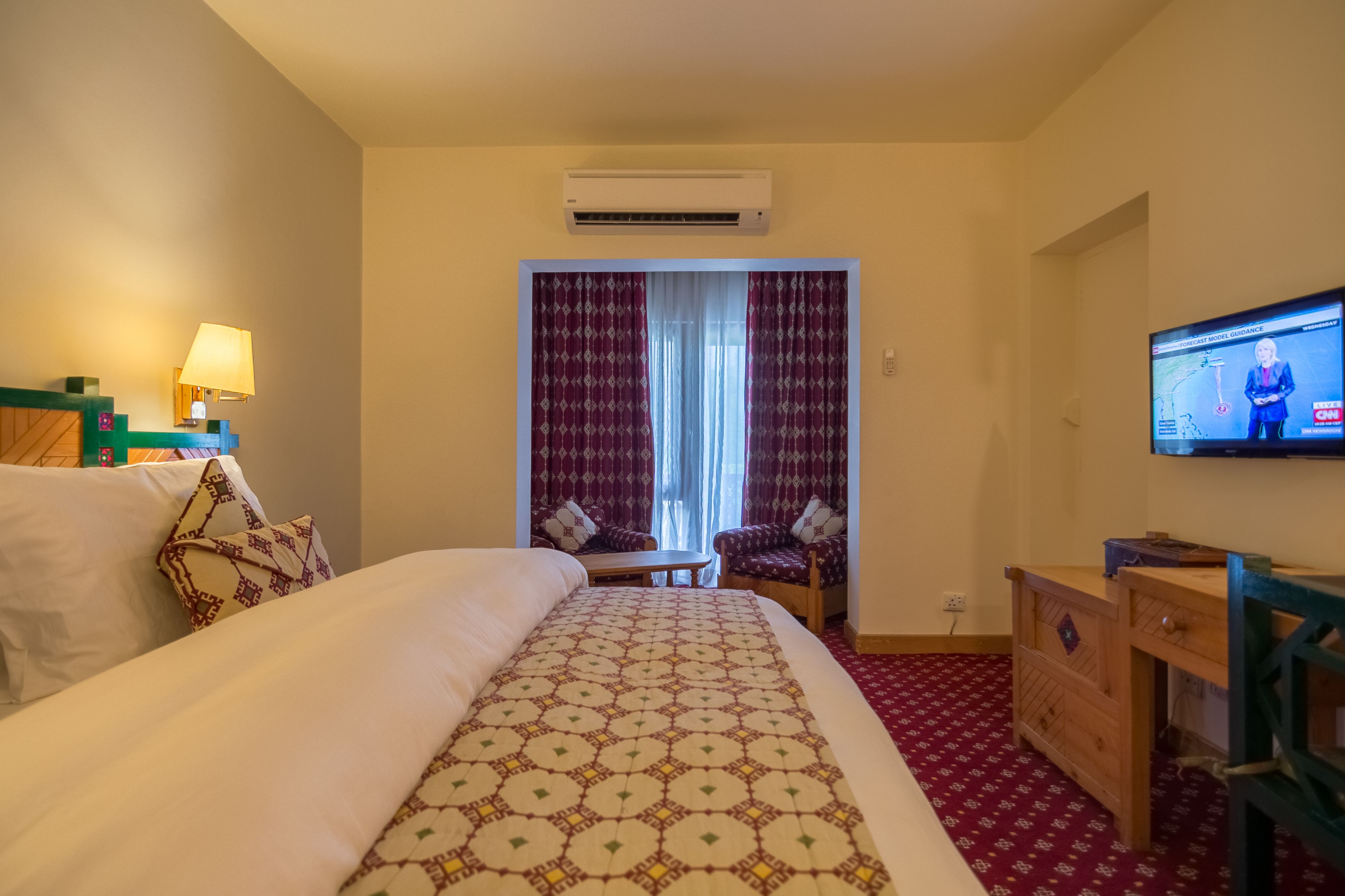 Una habitación de hotel con una cama, un escritorio, un televisor y un ventanal con cortinas.